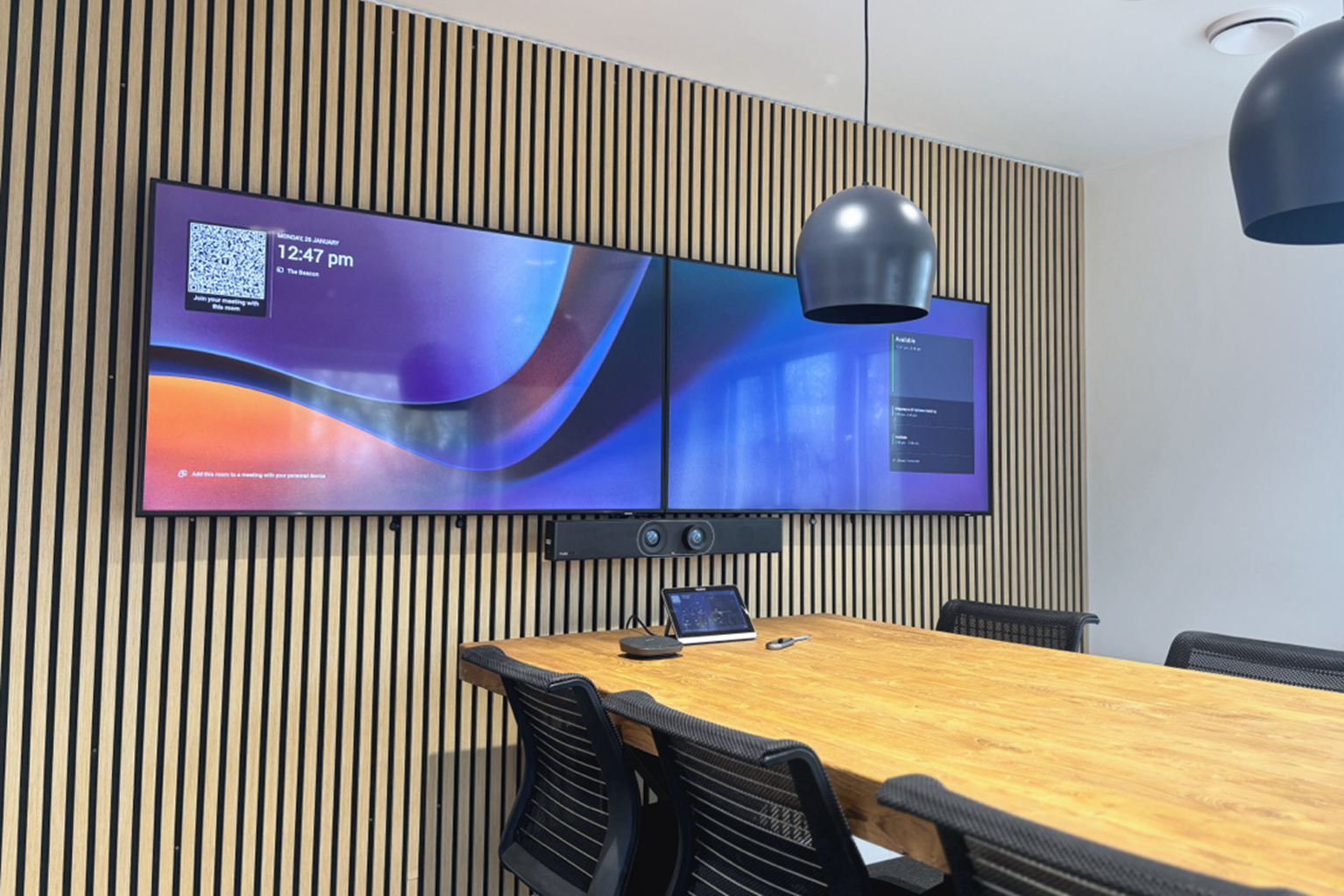 The Boardroom Space, duel monitors, desk and chairs, and conferencing equipment.